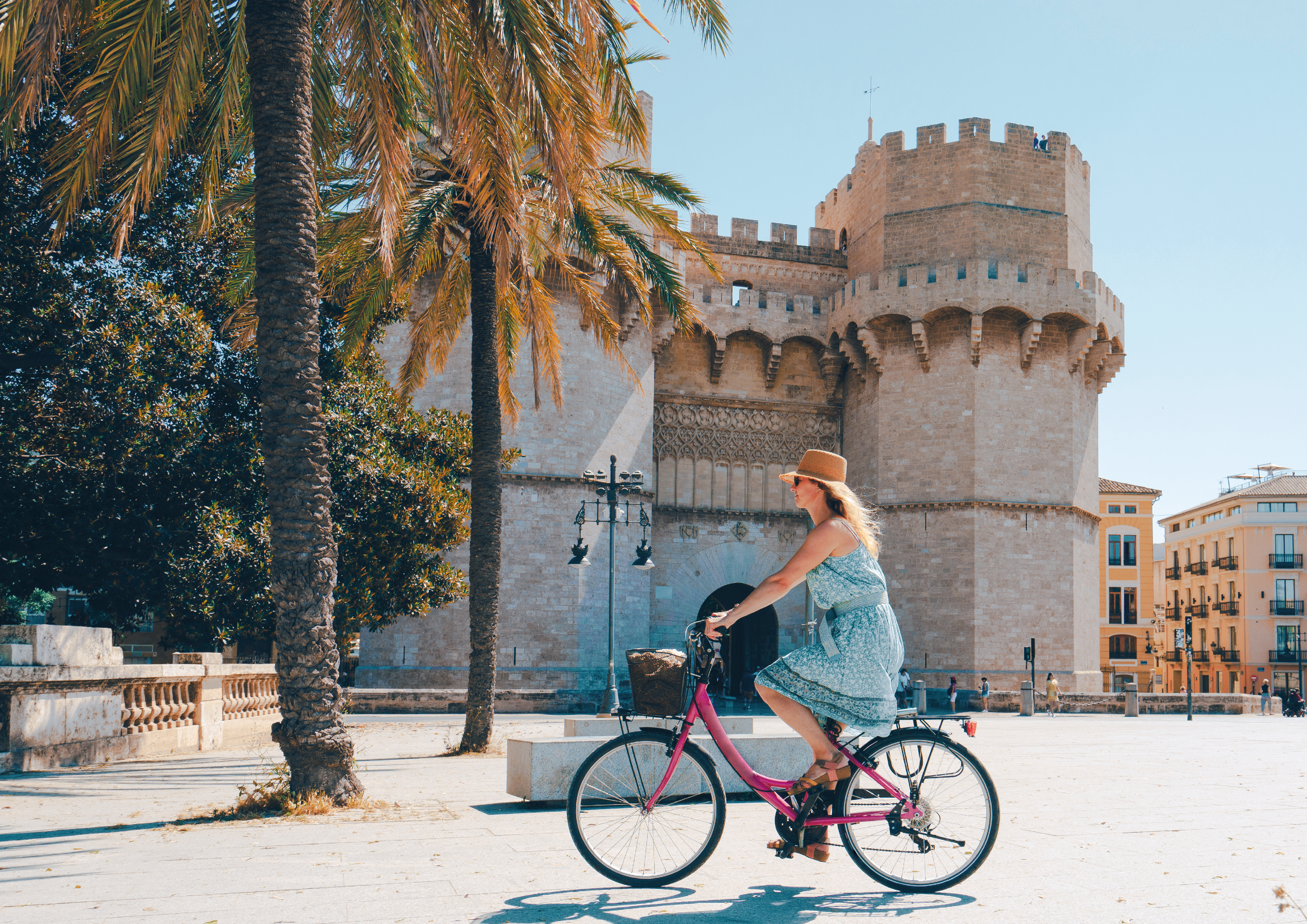 Frau auf einem pinken Fahrrad und mit Sonnenhut f&auml;hrt entspannt durch eine Altstadt
