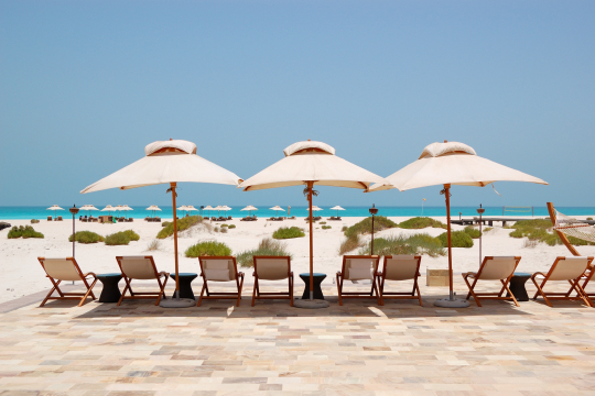 Hotelstrand auf Saadiyat Island in Abu Dhabi mit Holzstühlen, Sonnenschirmen und Liegen am Strand im Hintergrund das Meer